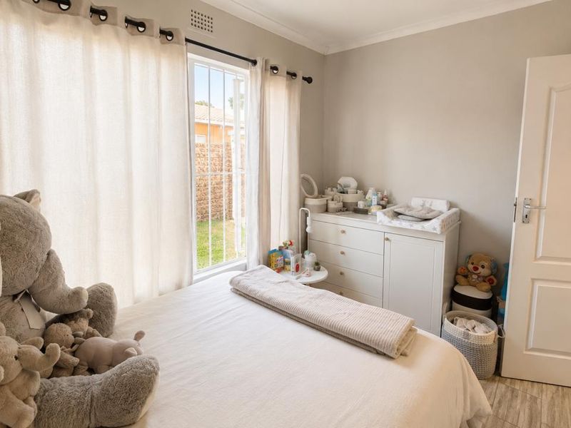 A well-lit bedroom featuring tiled flooring, neutral wall tones, and a window fitted with security bars, offering a comfortable and functional living space.
