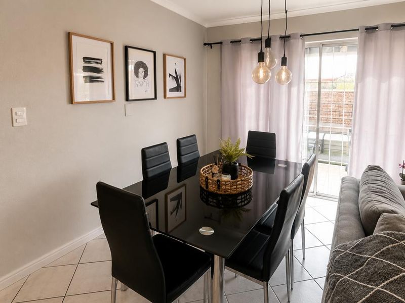 An open-plan dining area featuring ceramic floor tiles, modern pendant lighting, and a sliding glass door providing access to the outdoor space.