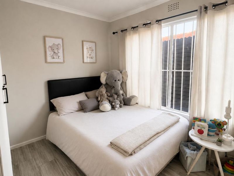 A well-maintained bedroom featuring light laminate flooring, neutral wall tones, and a window fitted with security bars.