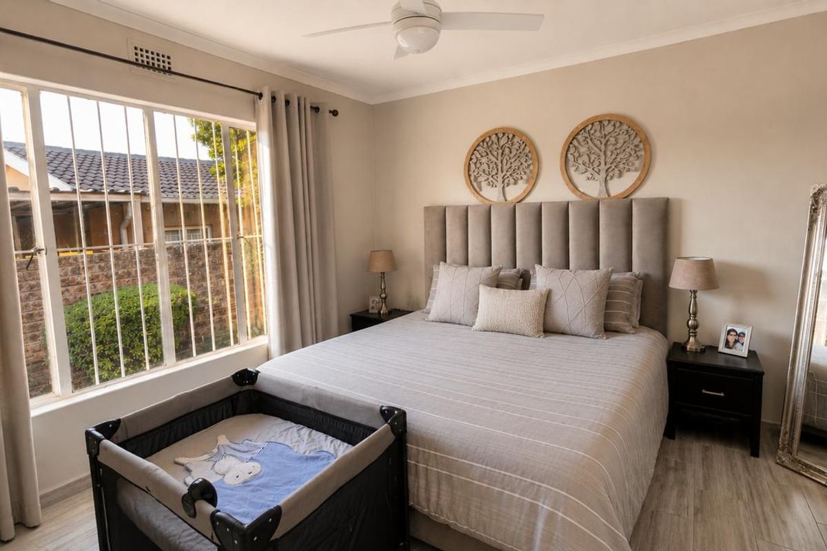 A well-maintained bedroom featuring neutral tones, laminate flooring, a ceiling fan, and large windows fitted with security bars.
