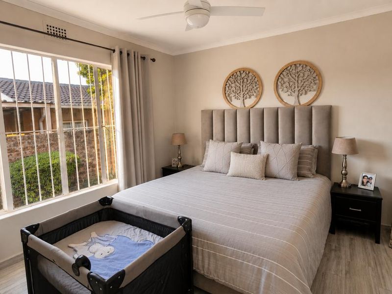 A well-maintained bedroom featuring neutral tones, laminate flooring, a ceiling fan, and large windows fitted with security bars.