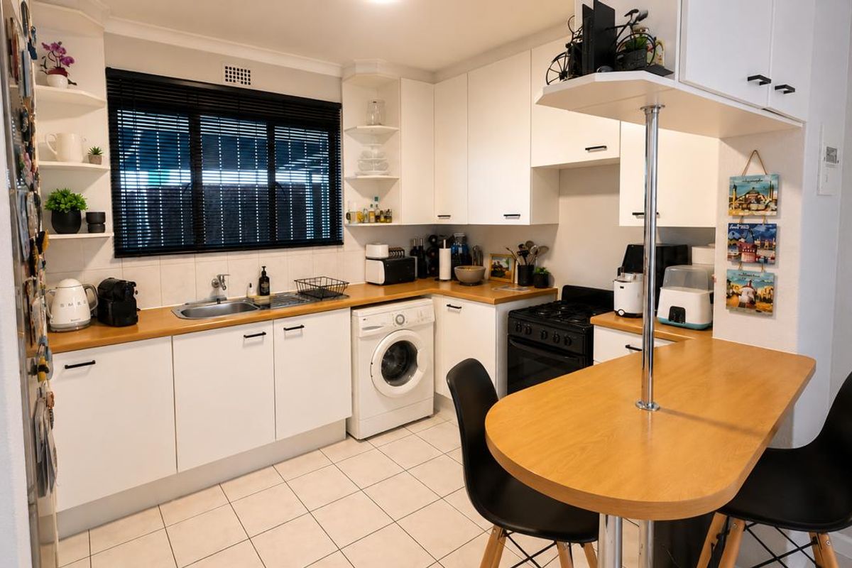 A functional kitchen featuring white cabinetry, wooden countertops, a breakfast bar, and integrated appliances including a washing machine and oven.
