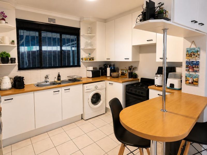 A functional kitchen featuring white cabinetry, wooden countertops, a breakfast bar, and integrated appliances including a washing machine and oven.