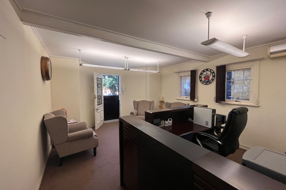 A functional commercial office space featuring neutral walls, carpeted flooring, built-in air conditioning, and natural light through timber-framed windows.
