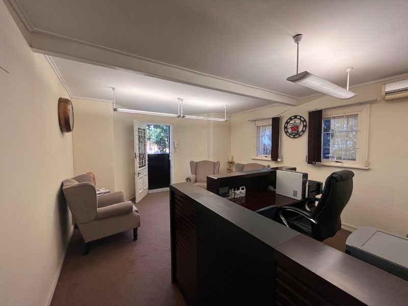 A functional commercial office space featuring neutral walls, carpeted flooring, built-in air conditioning, and natural light through timber-framed windows.