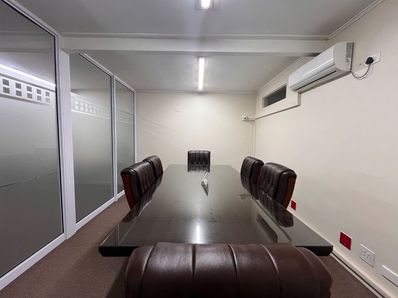 A professional office boardroom featuring frosted glass partitions, carpeted flooring, and a wall-mounted split-system air conditioning unit.