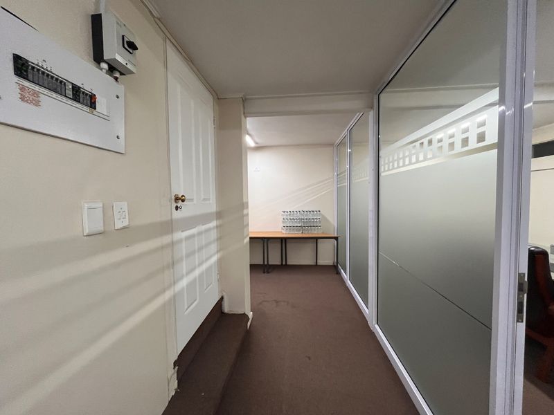 A functional commercial hallway featuring a wall-mounted electrical distribution board, a panel door, and frosted glass partitions separating adjacent office spaces.
