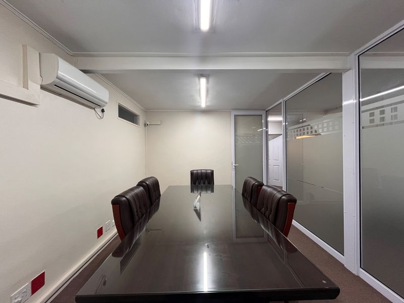 A professional meeting room featuring a glass partition wall, split-system air conditioning, and carpeted flooring, suitable for corporate use.