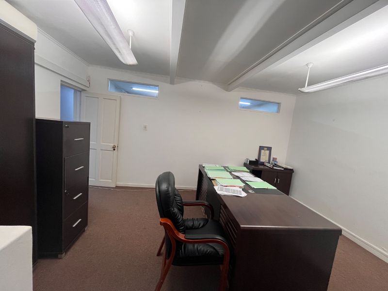 A functional office space featuring carpeted flooring, fluorescent lighting, and clerestory windows providing natural light.