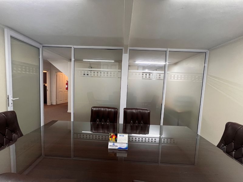 A professional office meeting room featuring frosted glass partitions, aluminum framing, and integrated lighting, providing a functional workspace environment.