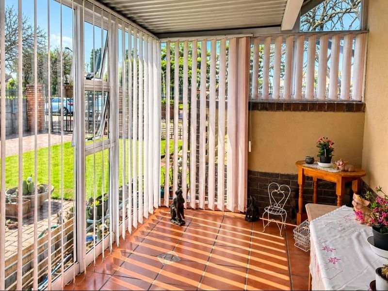 Enclosed patio area featuring tiled flooring, large windows with vertical blinds, and a corrugated roof, offering a bright and versatile transition space.
