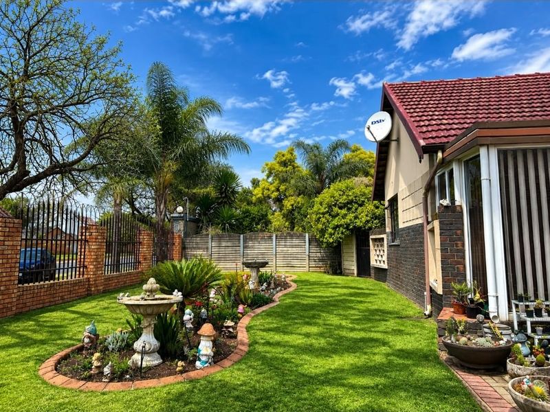 A well-maintained garden featuring a manicured lawn, brick-edged flower beds, a stone bird bath, and secure perimeter fencing.