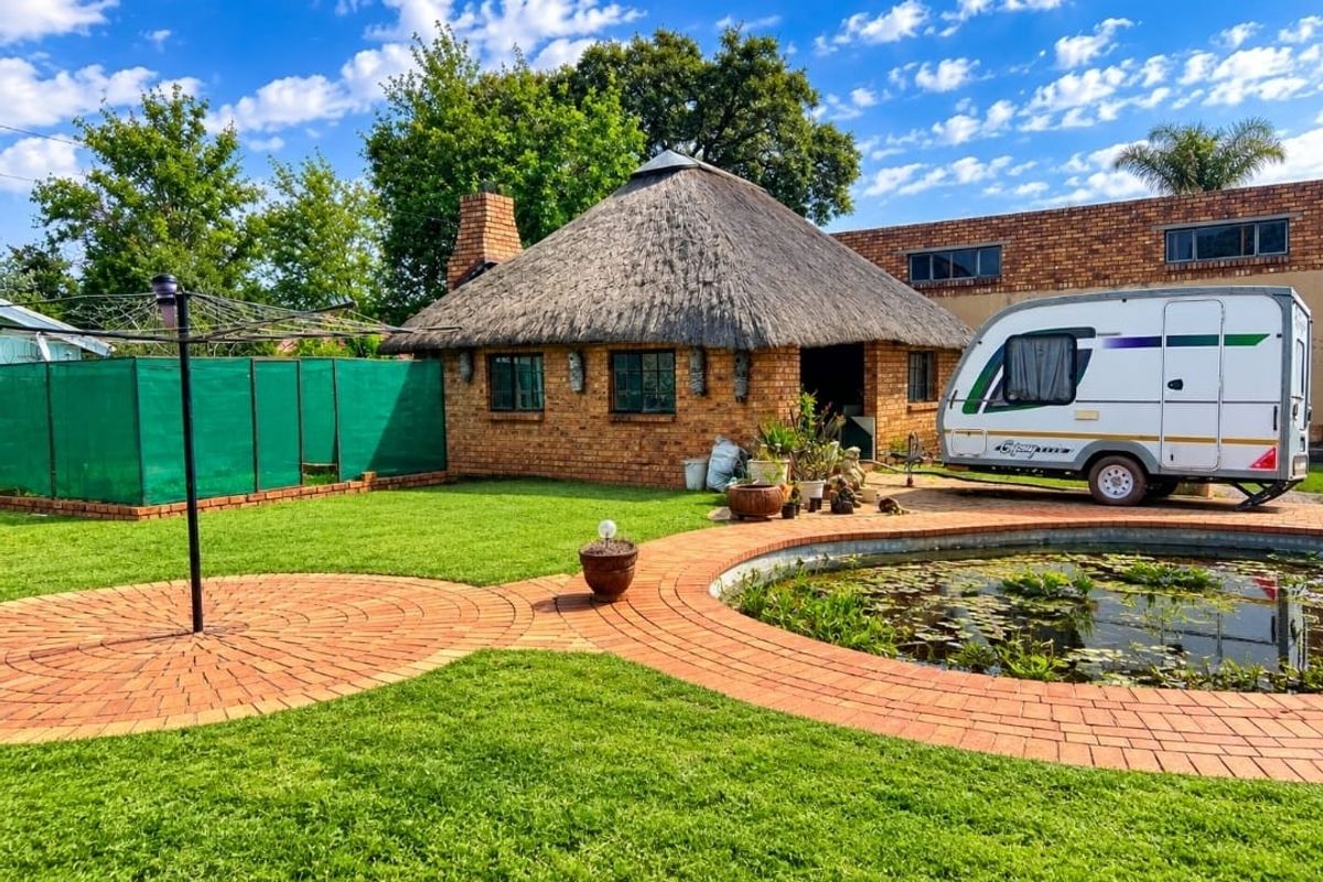 A well-maintained rear garden featuring a traditional thatch-roofed structure, brick paving, and a decorative pond.