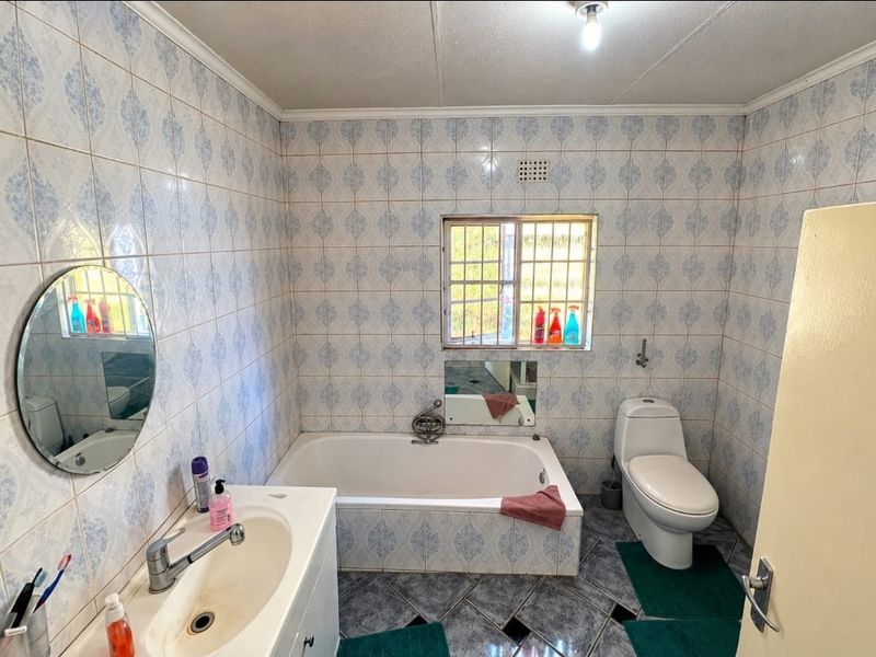 A functional bathroom featuring a built-in bathtub, toilet, and vanity basin with classic patterned wall tiles and dark floor tiles.