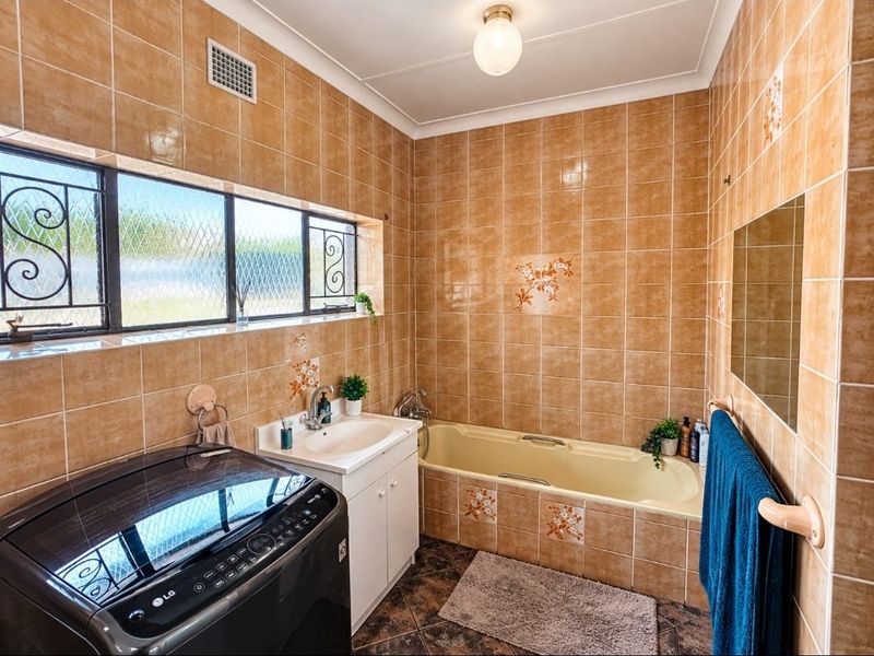 A functional bathroom featuring full-height wall tiling, a built-in bathtub, and a vanity basin with integrated laundry space.