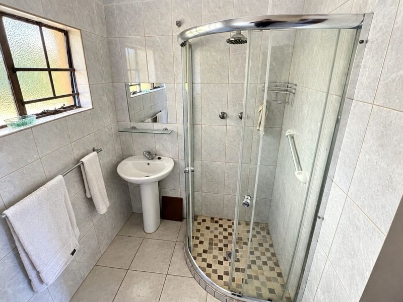 A functional bathroom featuring a pedestal basin, a curved glass shower enclosure, and neutral wall tiling throughout.