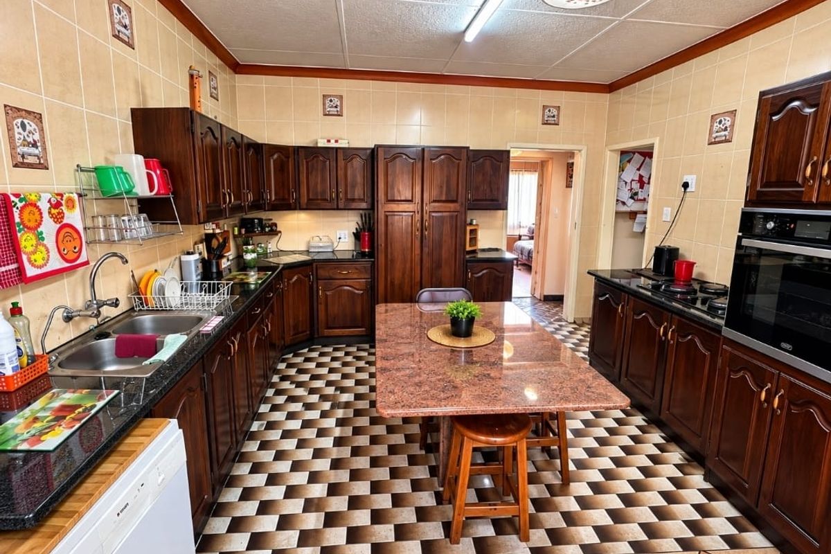 A functional kitchen featuring dark wood cabinetry, granite countertops, a built-in oven and hob, and a central island with integrated seating.