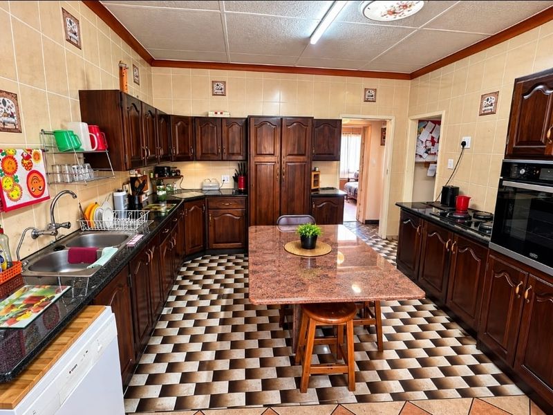 A functional kitchen featuring dark wood cabinetry, granite countertops, a built-in oven and hob, and a central island with integrated seating.