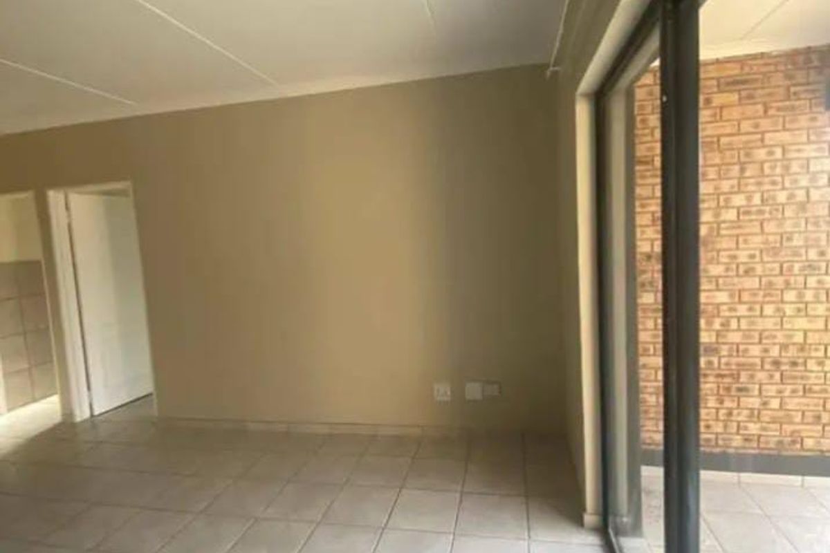 Spacious, empty living area featuring neutral tiled flooring and a large sliding glass door leading to an outdoor balcony with exposed brickwork.