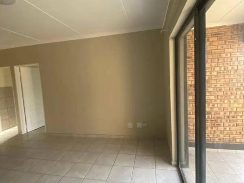 Spacious, empty living area featuring neutral tiled flooring and a large sliding glass door leading to an outdoor balcony with exposed brickwork.