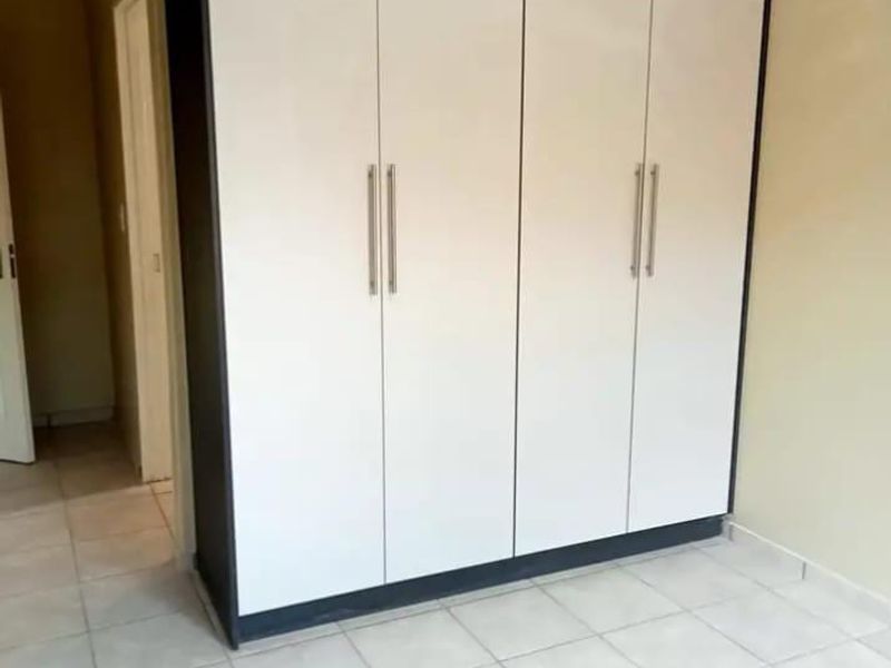 A clean, empty bedroom featuring neutral tiled flooring and modern, full-height built-in cupboards with a contrasting frame.