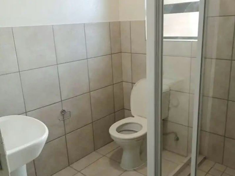 A functional bathroom featuring a pedestal basin, toilet, and a glass-enclosed shower with neutral ceramic tiling throughout.