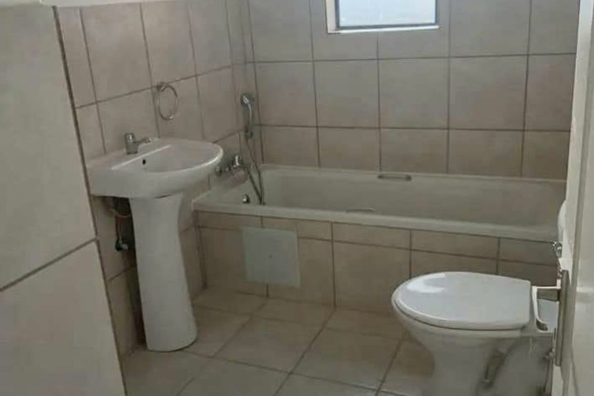 A functional bathroom featuring a pedestal basin, bathtub with handheld shower mixer, and toilet, finished with neutral wall and floor tiling.