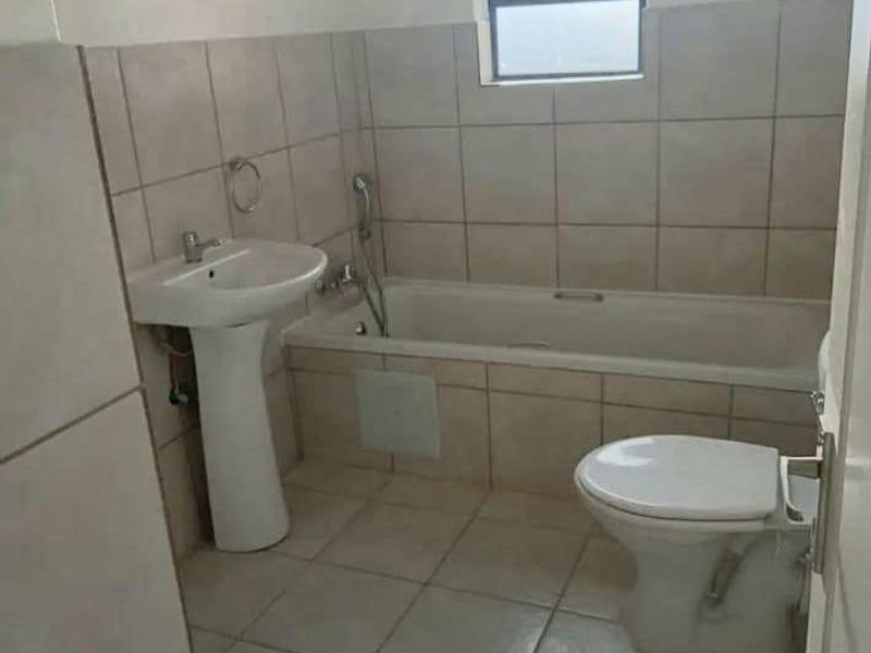 A functional bathroom featuring a pedestal basin, bathtub with handheld shower mixer, and toilet, finished with neutral wall and floor tiling.