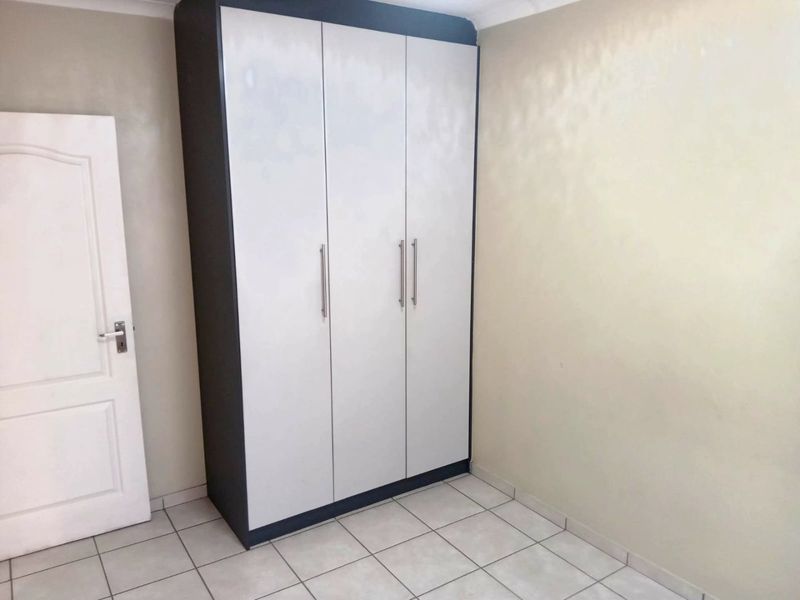 A clean, empty bedroom featuring neutral tiled flooring and a modern built-in wardrobe with white doors and dark framing.