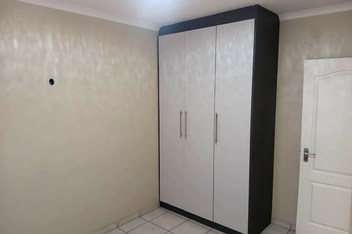 A clean, empty bedroom featuring neutral wall tones, tiled flooring, and a modern built-in wardrobe with contrasting dark and light finishes.