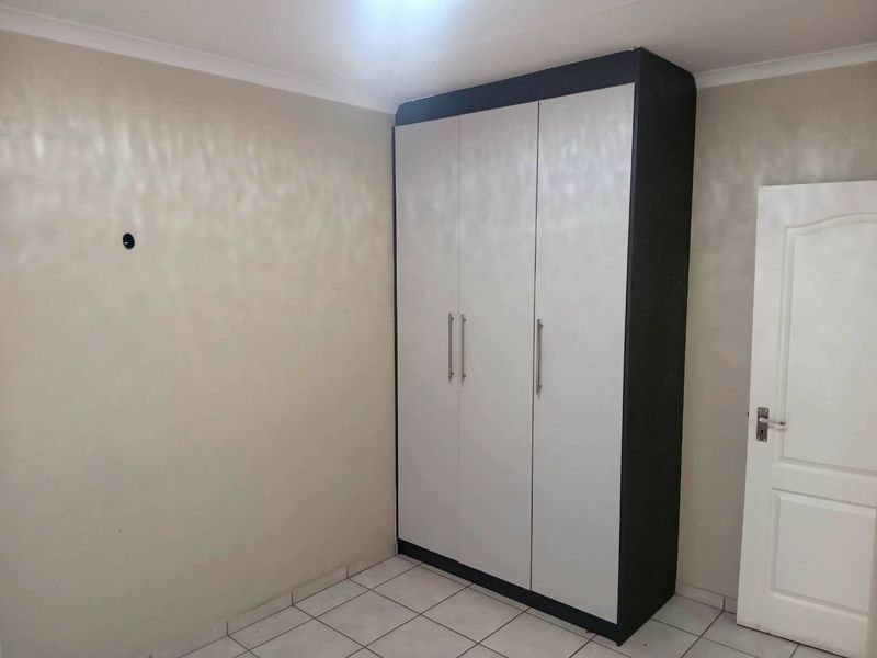 A clean, empty bedroom featuring neutral wall tones, tiled flooring, and a modern built-in wardrobe with contrasting dark and light finishes.
