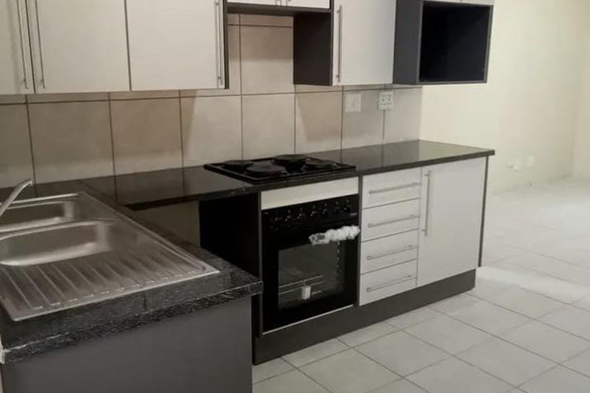 A clean, modern kitchen featuring built-in cabinetry, a double sink, and a built-in oven with hob, finished with neutral tiled flooring and backsplash.