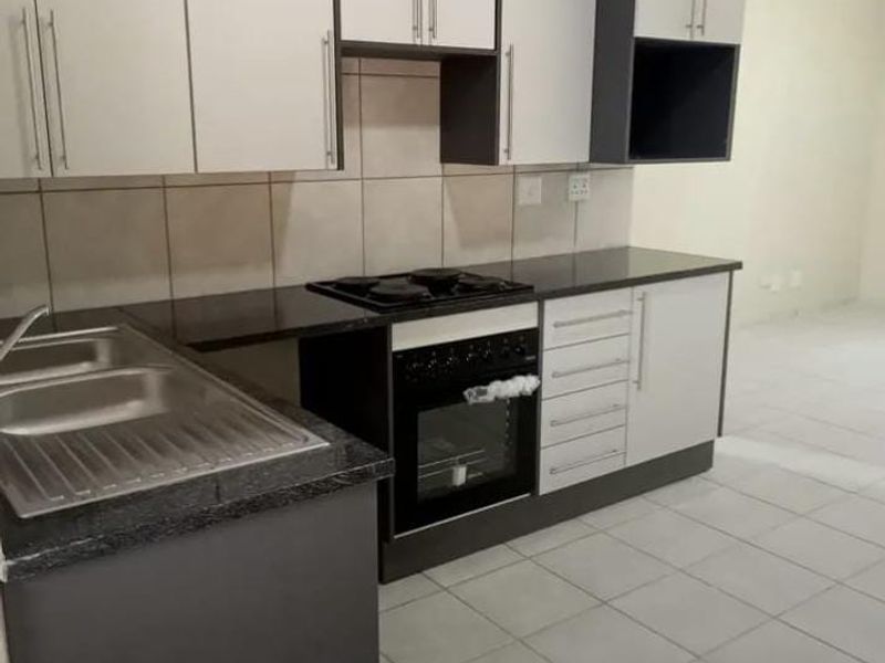 A clean, modern kitchen featuring built-in cabinetry, a double sink, and a built-in oven with hob, finished with neutral tiled flooring and backsplash.