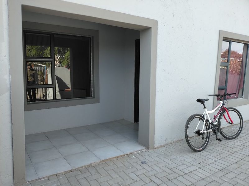 A covered patio area featuring tiled flooring and modern aluminium window frames, providing a clean and functional outdoor entrance space.