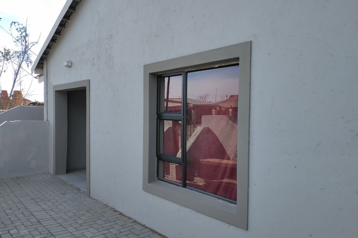 A view of the rear exterior wall featuring a paved walkway, aluminium window frame, and exterior lighting.