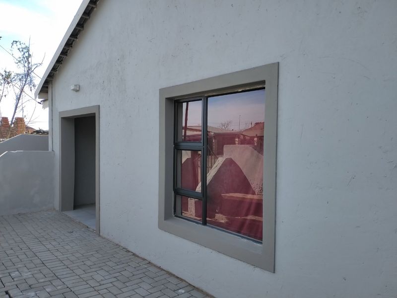 A view of the rear exterior wall featuring a paved walkway, aluminium window frame, and exterior lighting.