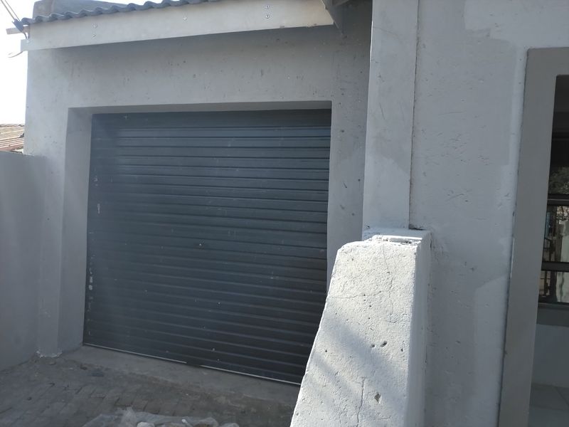 Exterior view of a single garage featuring a dark roller shutter door and concrete masonry construction with visible signs of wear and unfinished plastering.
