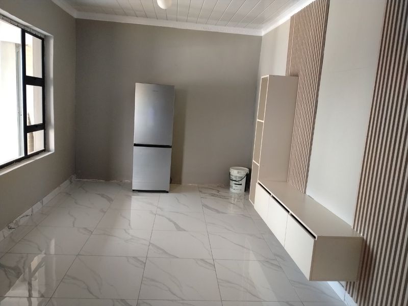 A bright, modern living area featuring large marble-look floor tiles, a decorative slatted timber wall feature, and sleek built-in floating cabinetry.