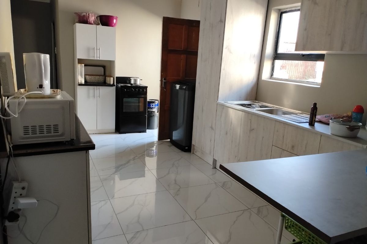 A functional kitchen featuring modern marble-look floor tiles, light wood-grain cabinetry, and a stainless steel sink with ample counter space.