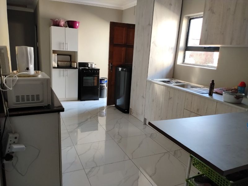 A functional kitchen featuring modern marble-look floor tiles, light wood-grain cabinetry, and a stainless steel sink with ample counter space.