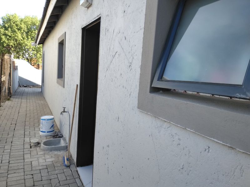 Side exterior view of the house featuring a paved walkway, external utility sink, and modern aluminium window frames.