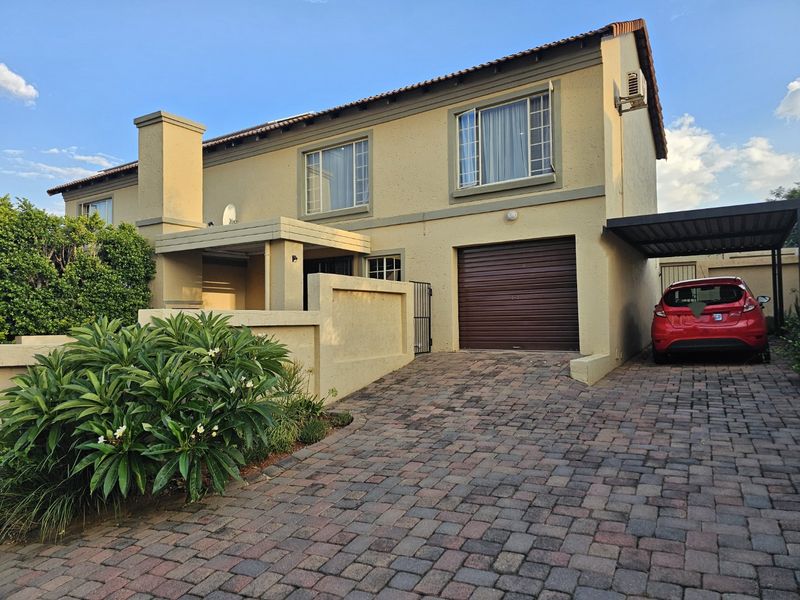 Front elevation of a double-story townhouse featuring a paved driveway, single garage, and attached carport.
