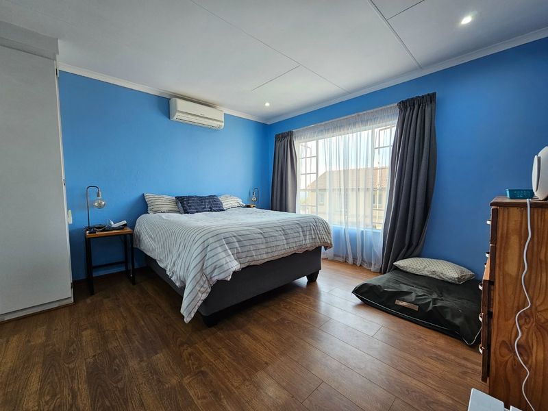 A well-lit bedroom featuring laminate flooring, a built-in wardrobe, and a wall-mounted split-system air conditioner.