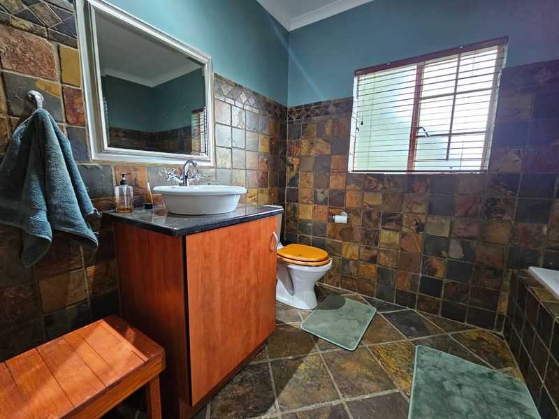 A bathroom featuring natural slate wall and floor tiling, a vessel sink with a granite vanity top, and a built-in bathtub.
