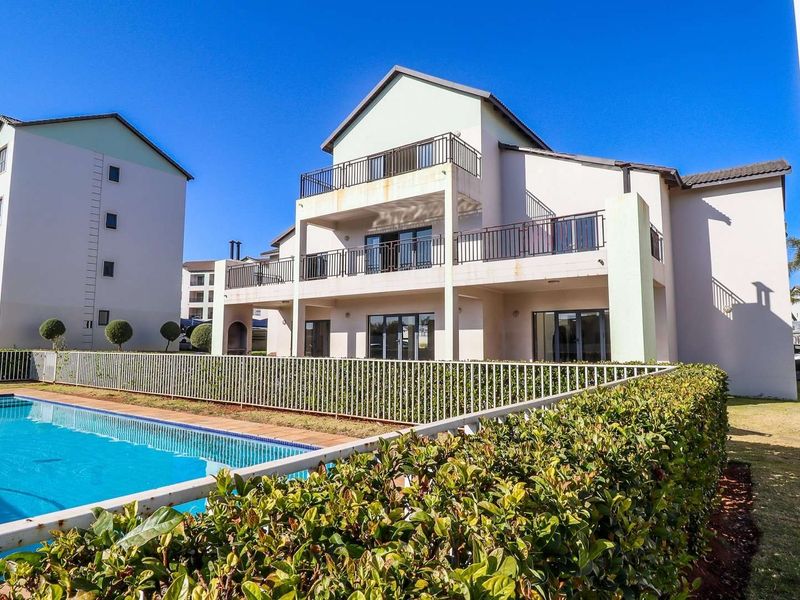 Exterior view of an apartment complex featuring a swimming pool, landscaped garden areas, and multi-level balconies with metal railings.