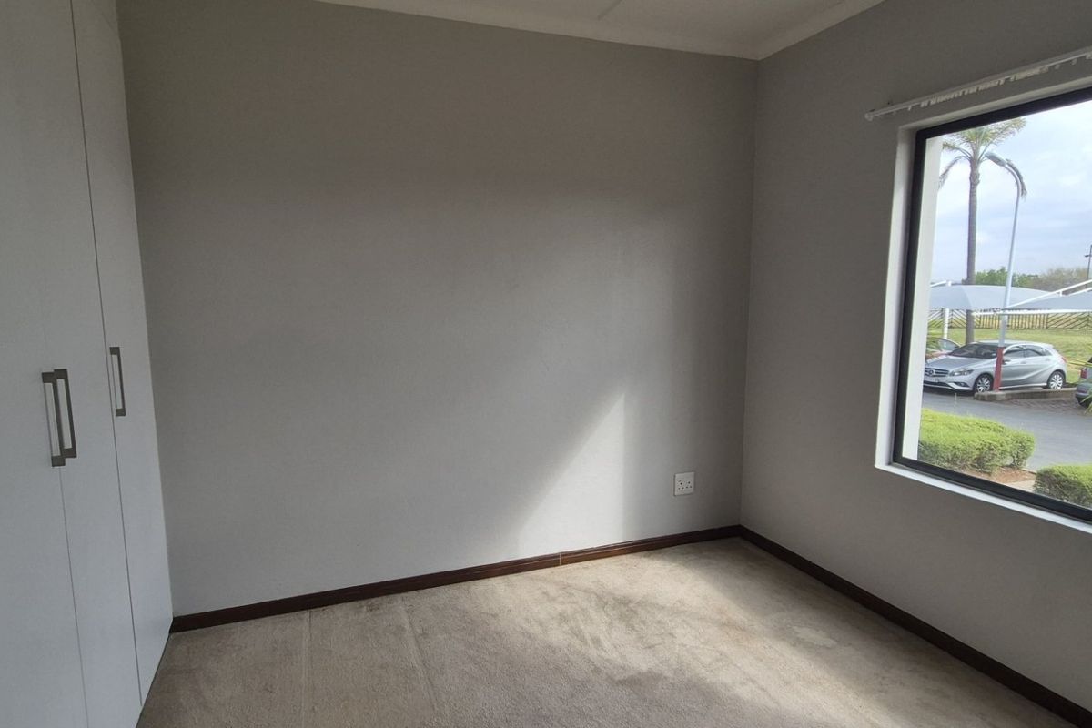 A bright, empty bedroom featuring neutral walls, carpeted flooring, and ample built-in cupboard storage with a window view.