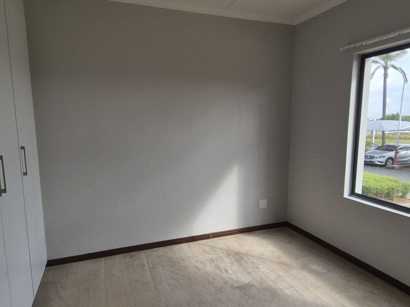 A bright, empty bedroom featuring neutral walls, carpeted flooring, and ample built-in cupboard storage with a window view.