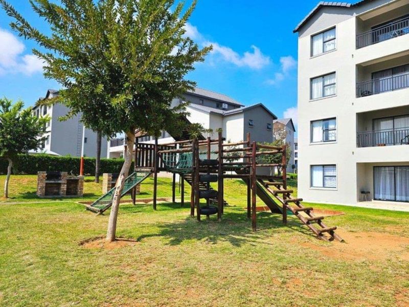 Communal garden area featuring a playground, brick braai facility, and views of the apartment building facade with private balconies.