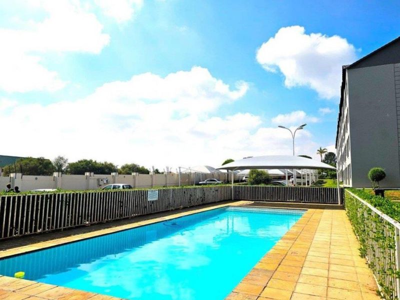 Communal swimming pool area featuring a tiled deck, perimeter fencing, and a shade sail structure for outdoor relaxation.