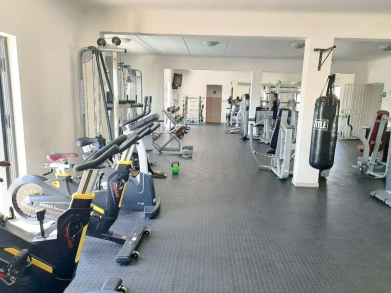 A spacious, well-equipped residential gym featuring durable rubberized flooring, recessed lighting, and structural support columns.